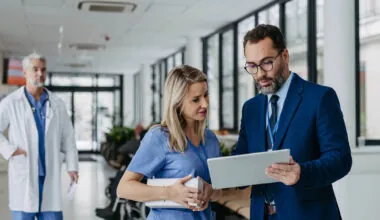 Pharmaceutical sales representative presenting new product to doctors in holding box with pills. Presenting new pharmaceutical product, drugs, medication.Hospital director, manager in private medical clinic showing something on tablet.