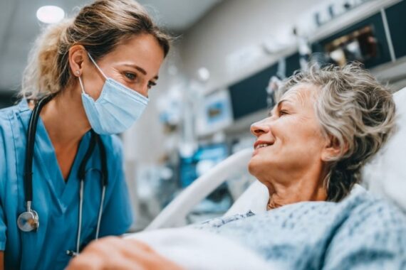 Nurse wearing mask next to patient in hospital bed. Patient is an older woman